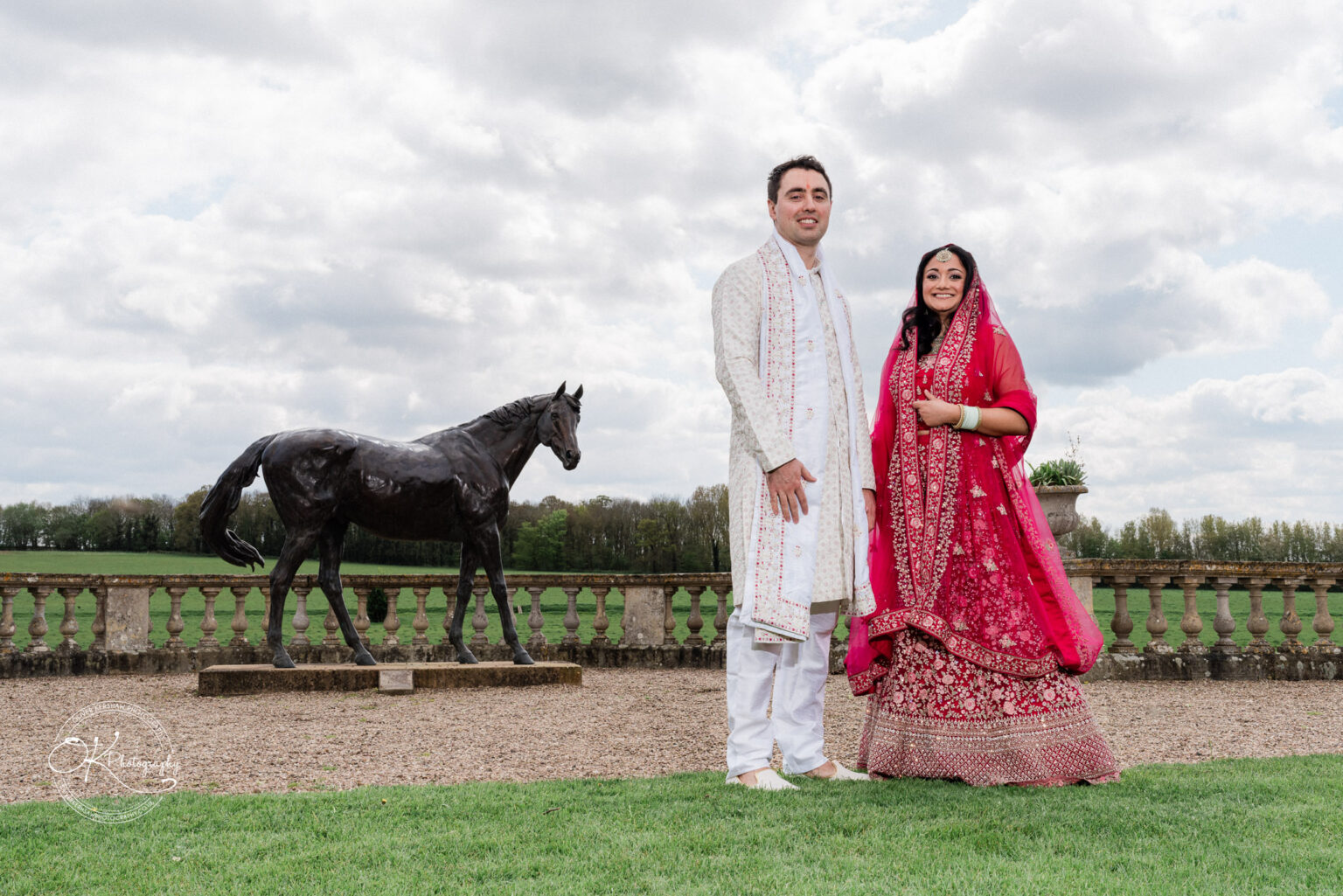 Bride and groom posing outdoors with a horse statue in the background.