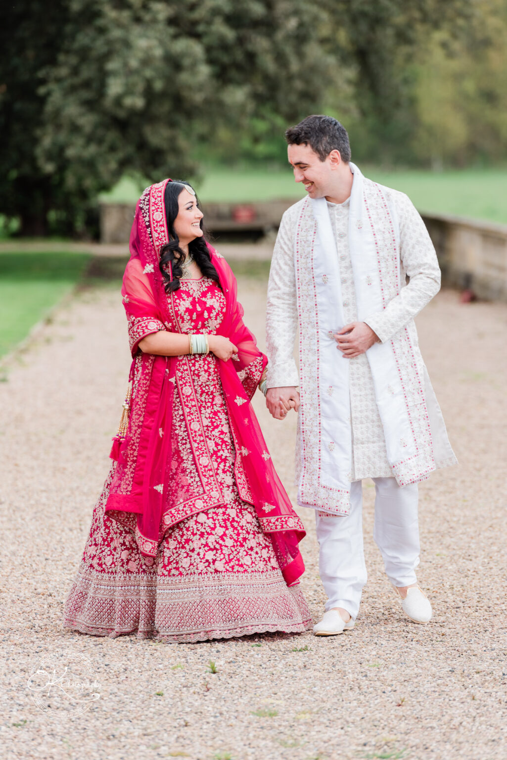 Bride and groom walking hand in hand outdoors, smiling at each other.