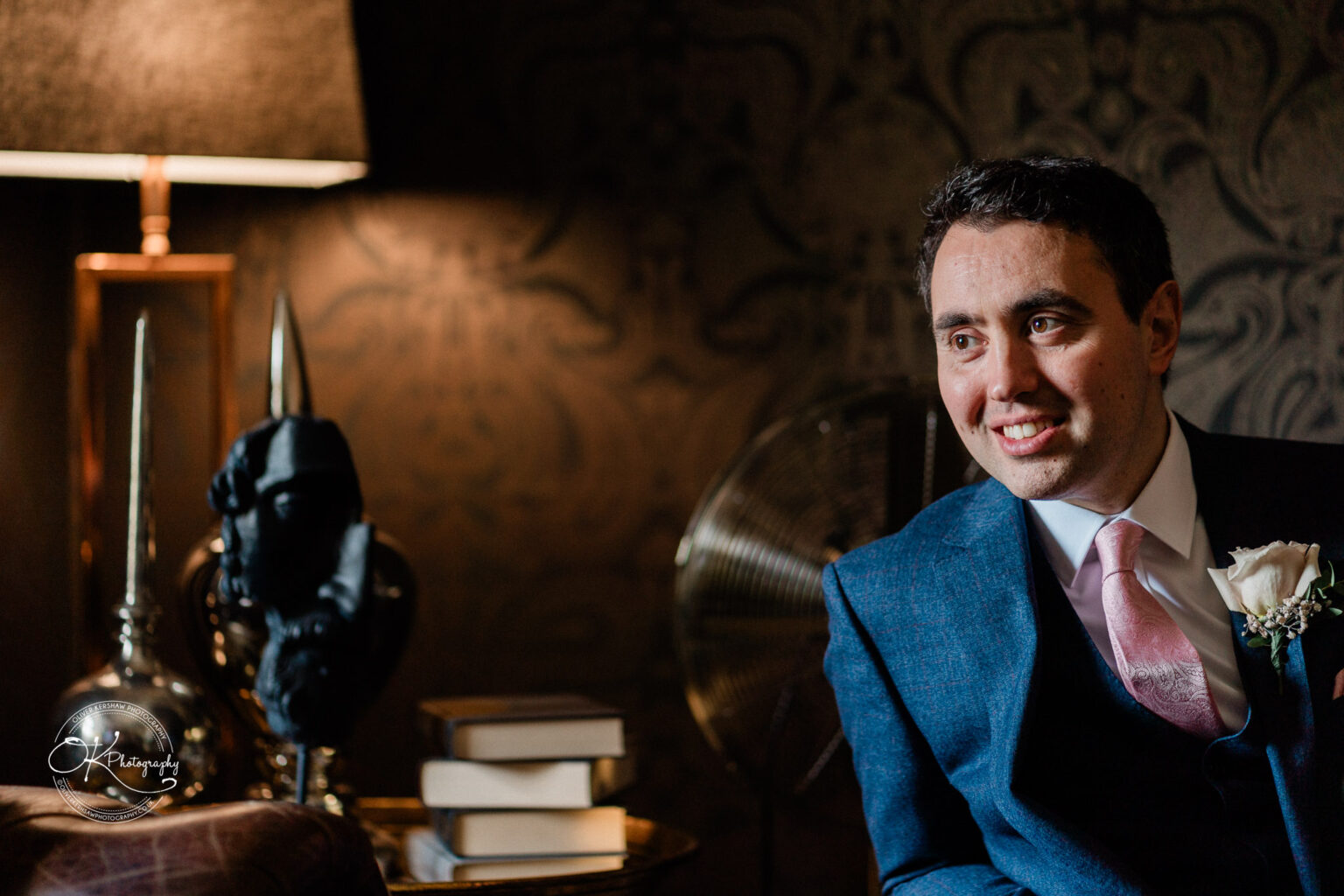 Groom sitting in a cozy, warmly lit room, smiling.