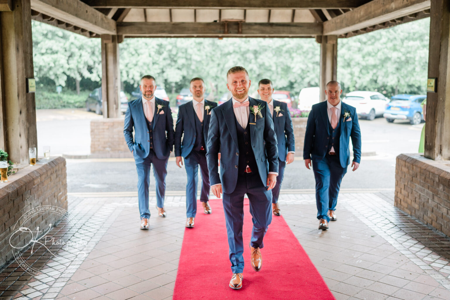 Groom and groomsmen in blue suits walking on a red carpet.
