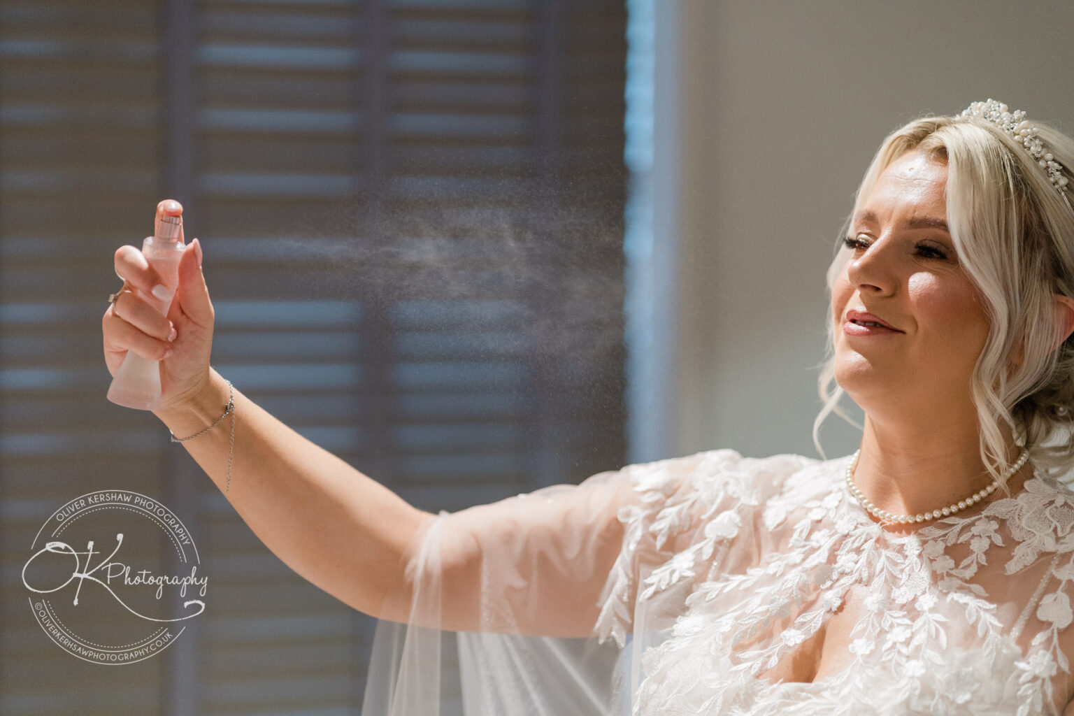 Woman in a bridal gown spraying perfume while preparing for her wedding.