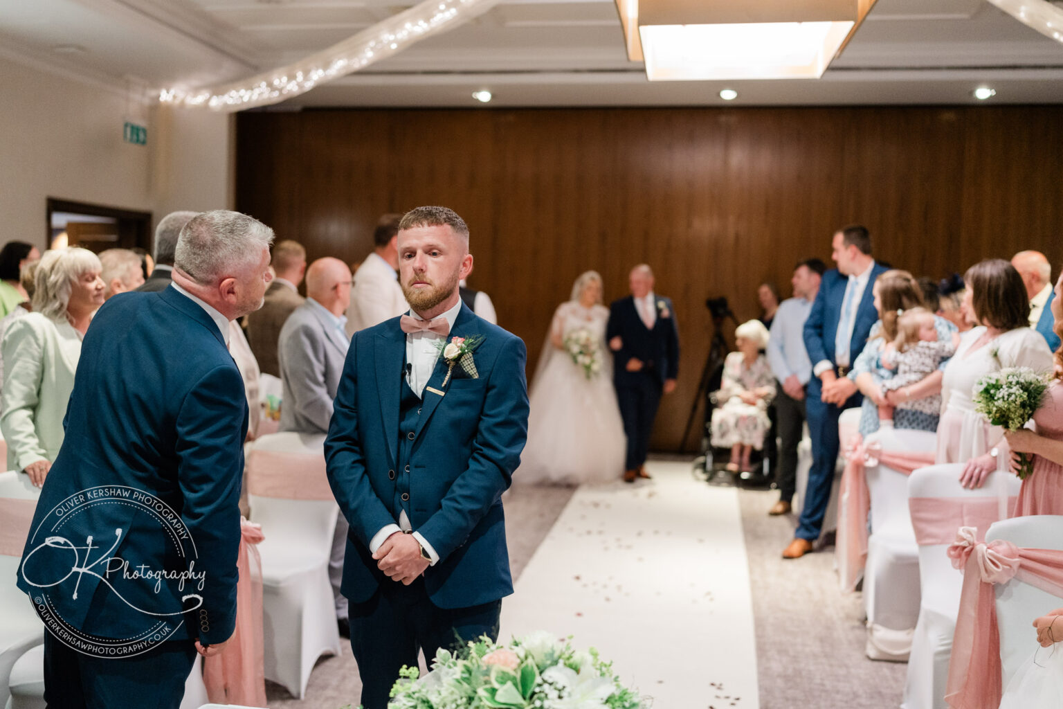 Groom standing at the altar waiting for the bride, surrounded by guests in a decorated wedding venue.