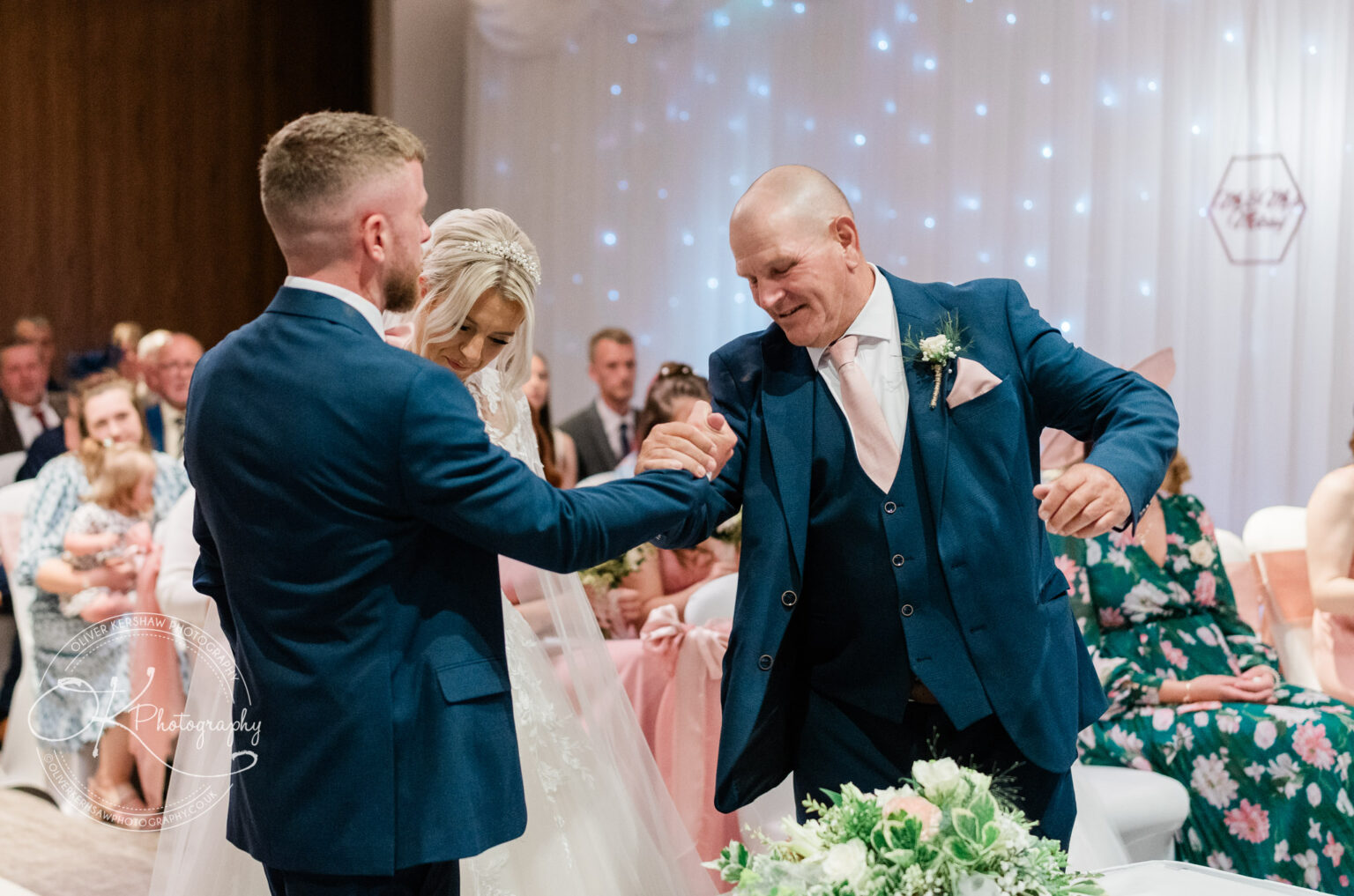 Man in a blue suit shaking hands with another man during a wedding ceremony.