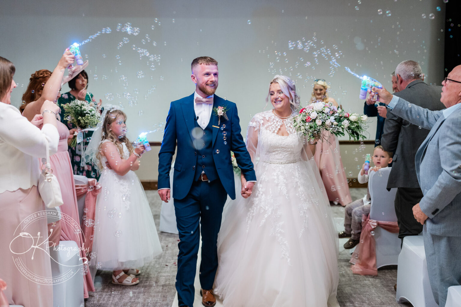 Bride and groom walking hand-in-hand down the aisle surrounded by guests blowing bubbles.
