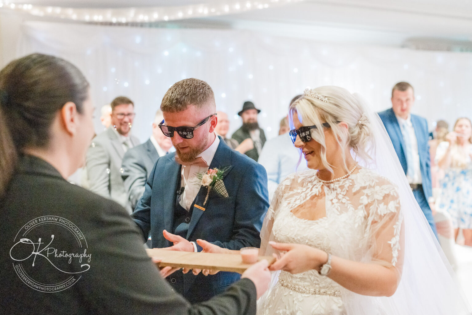 Bride and groom wearing sunglasses during wedding ceremony, with groom holding a tray.