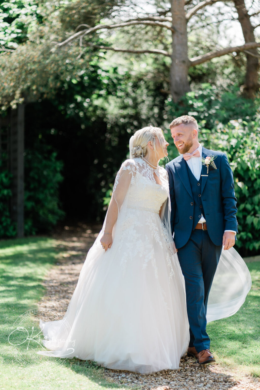 Bride and groom smiling and walking outdoors on a sunny day.