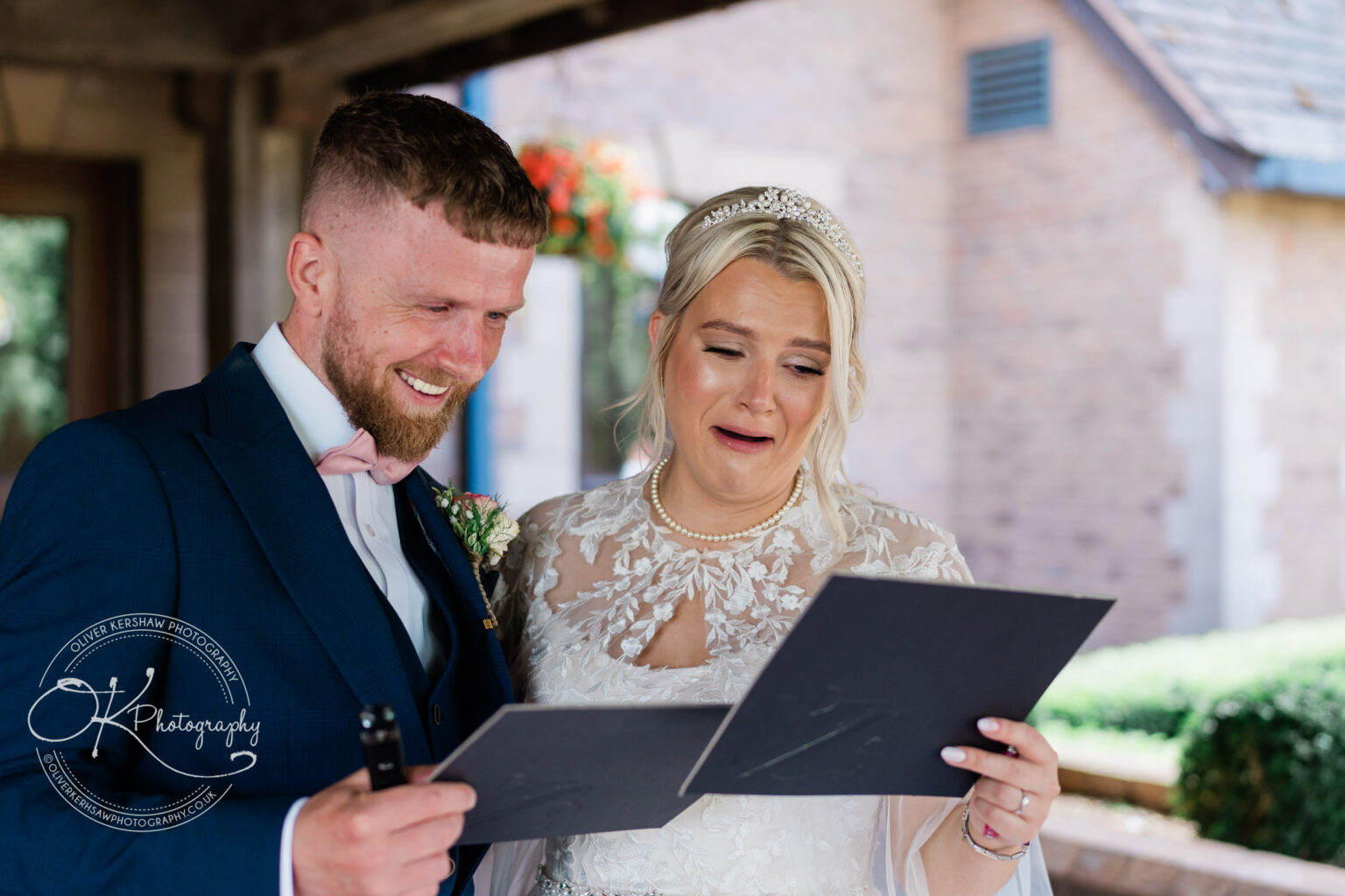 Bride and groom emotionally reading letters, dressed in wedding attire while standing together outdoors.