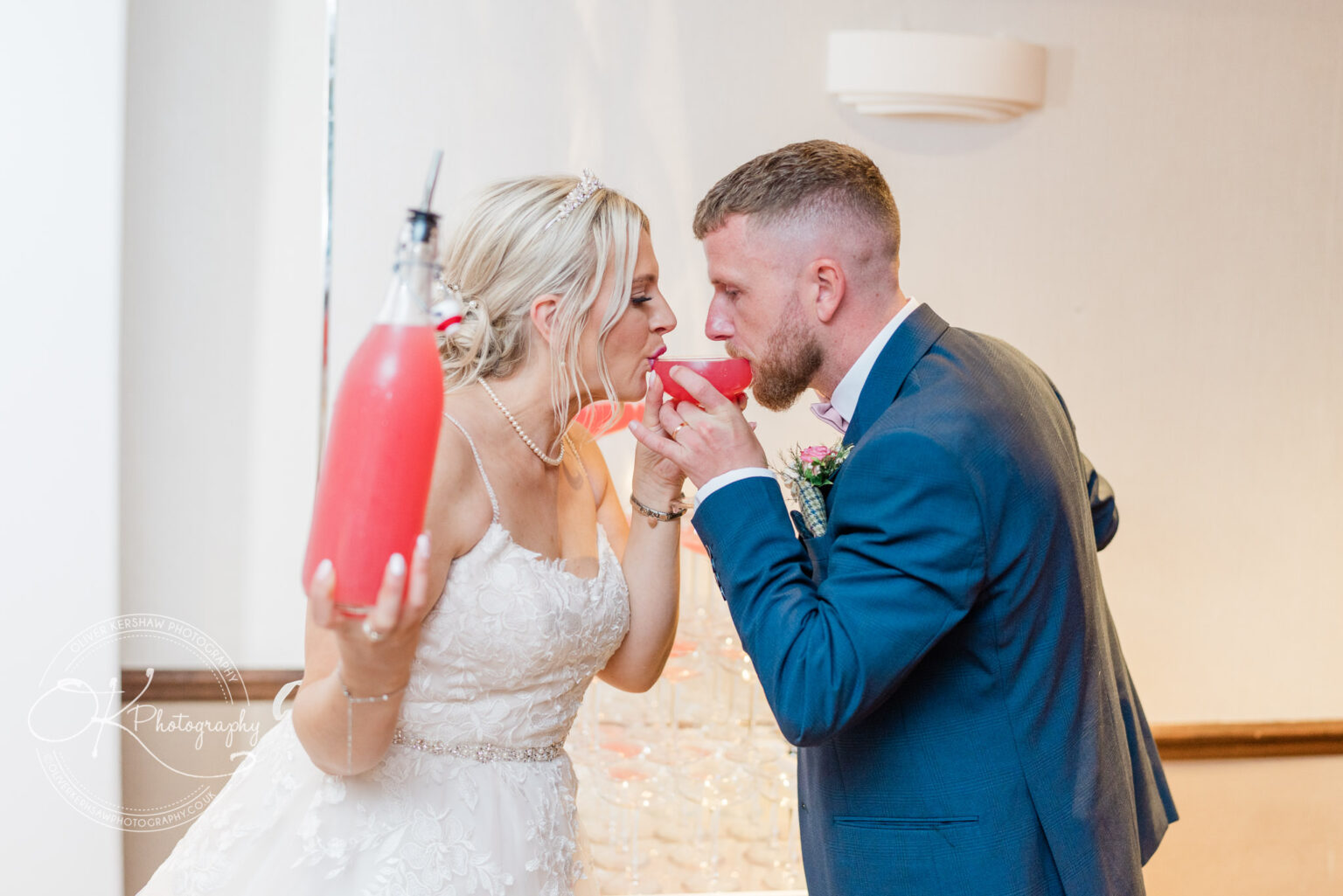 A bride and groom drink from the same cocktail while standing close together.