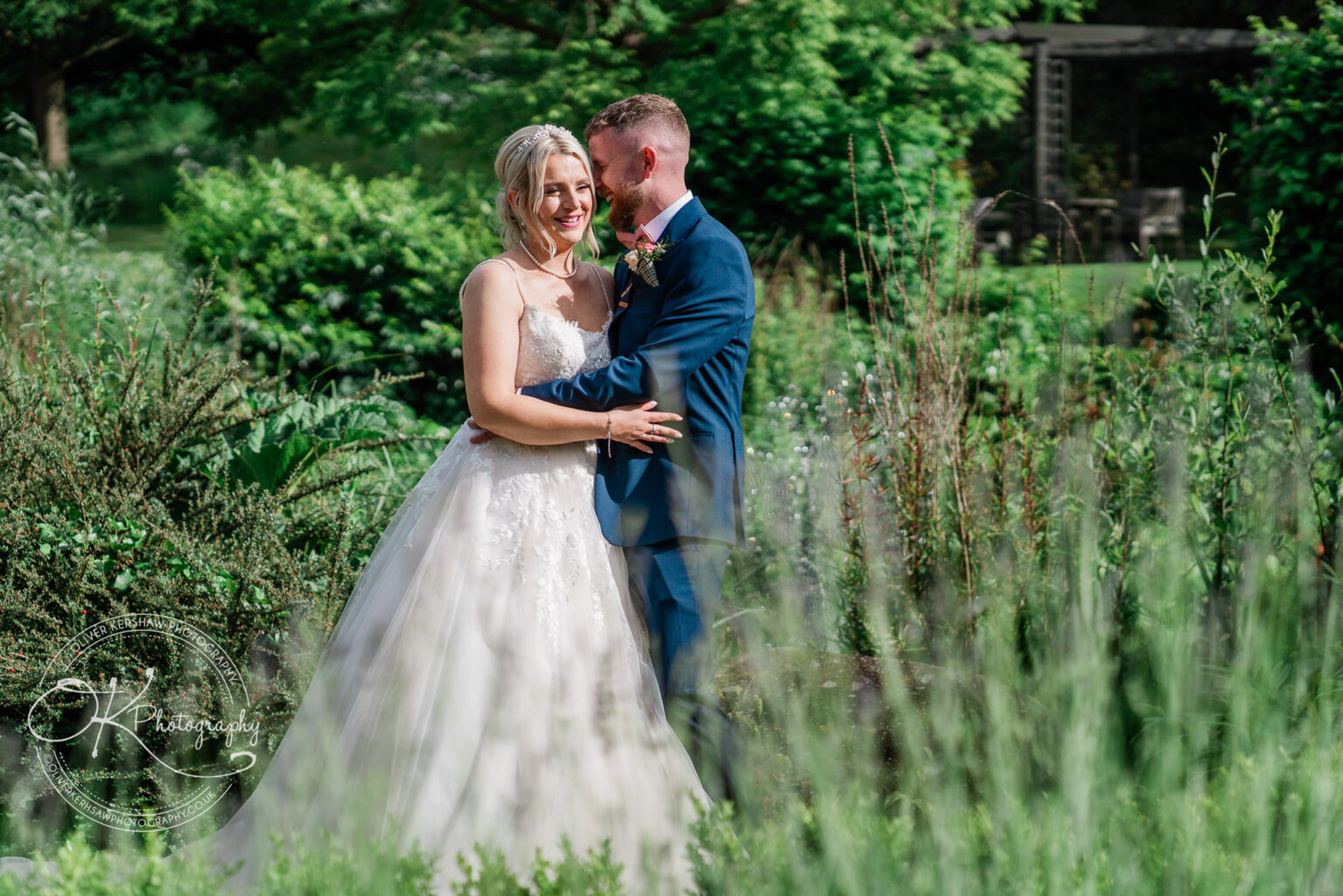 Bride and groom smiling and embracing in a lush garden setting.