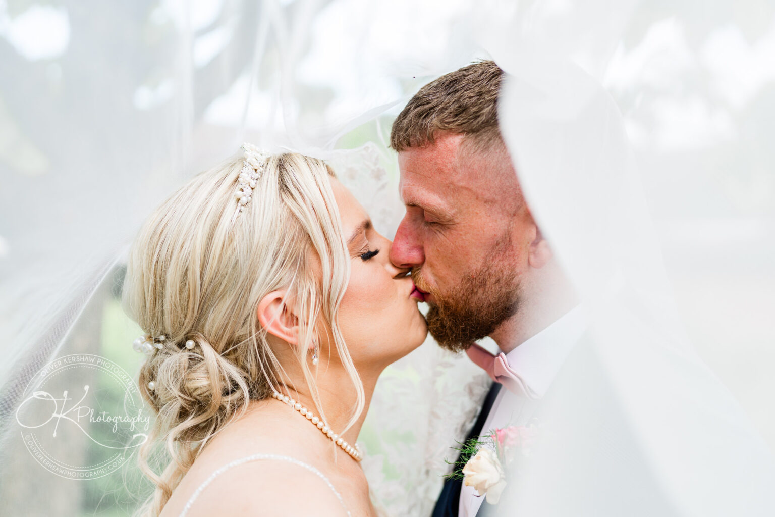 Bride and groom kissing beneath a veil.