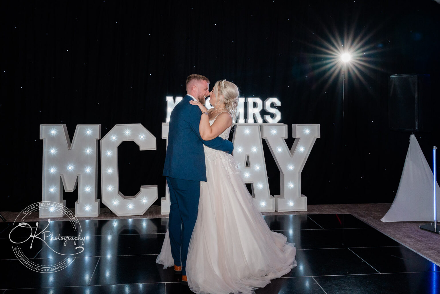 Bride and groom dancing in front of illuminated "MCILROY" sign at their wedding reception.