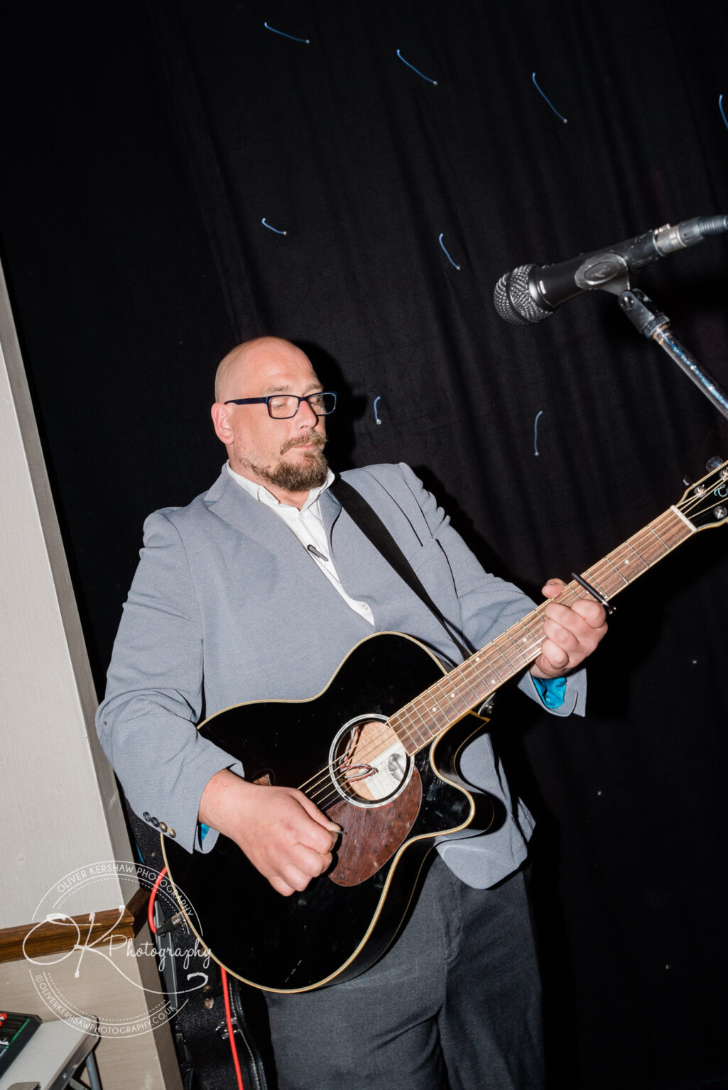 A man playing an acoustic guitar on stage next to a microphone.