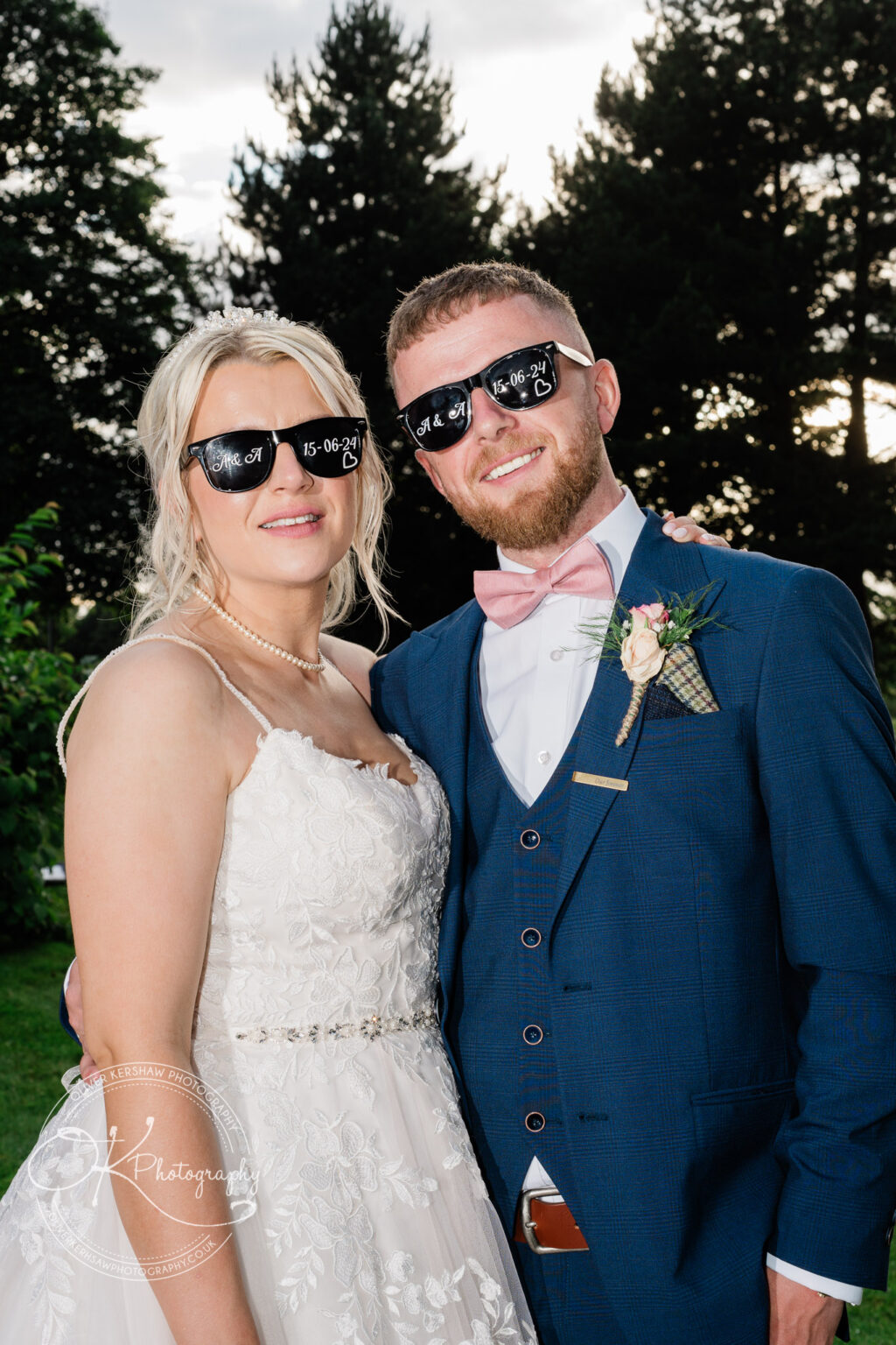 Bride and groom wearing personalised sunglasses, standing outdoors with trees in the background.