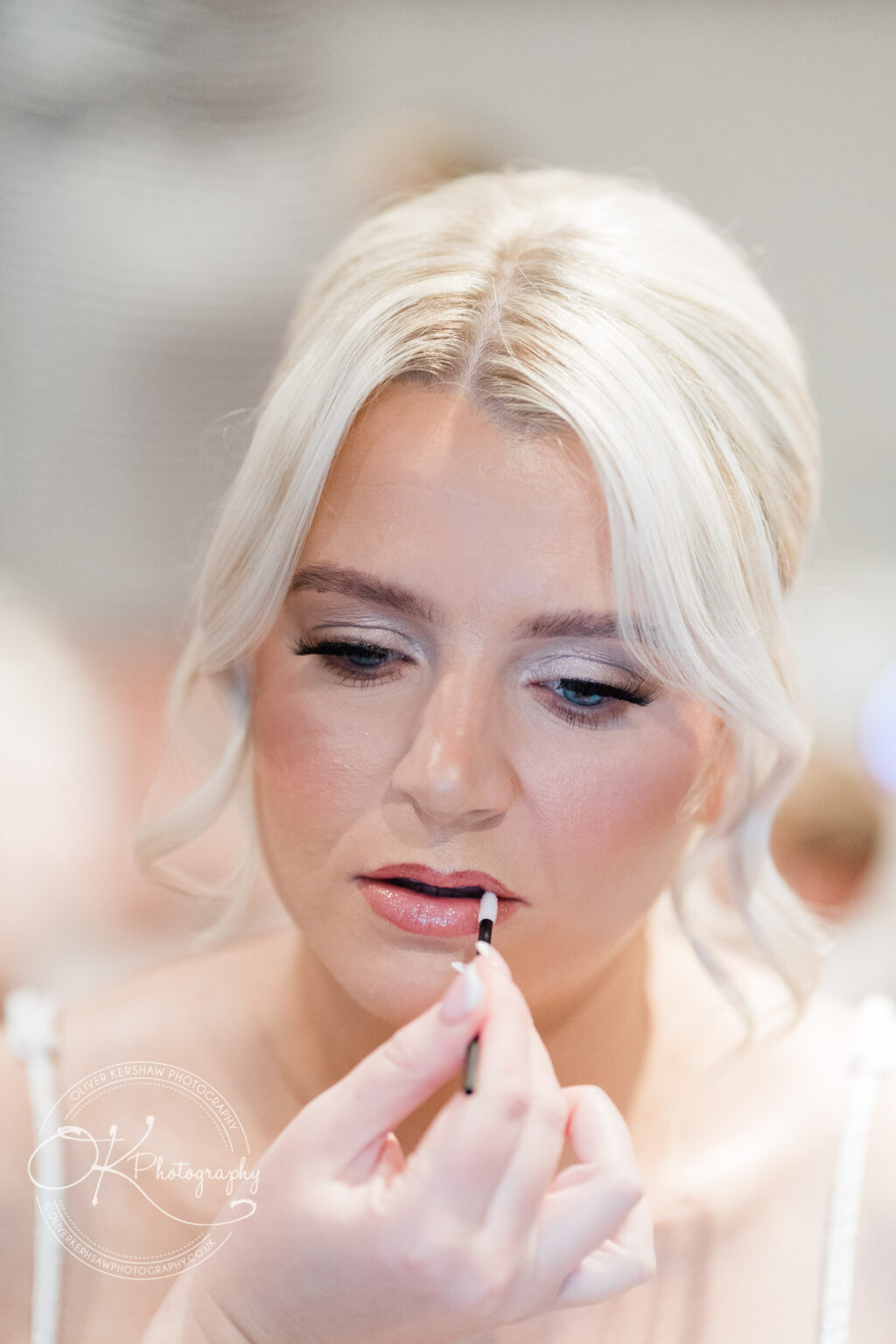 A woman applying lip gloss with a focused expression.