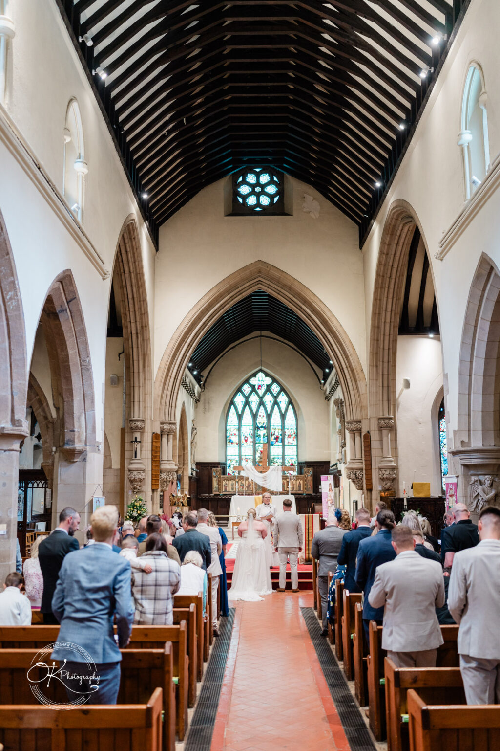 A wedding ceremony taking place in a church, featuring a bride and groom at the altar with guests seated in pews.