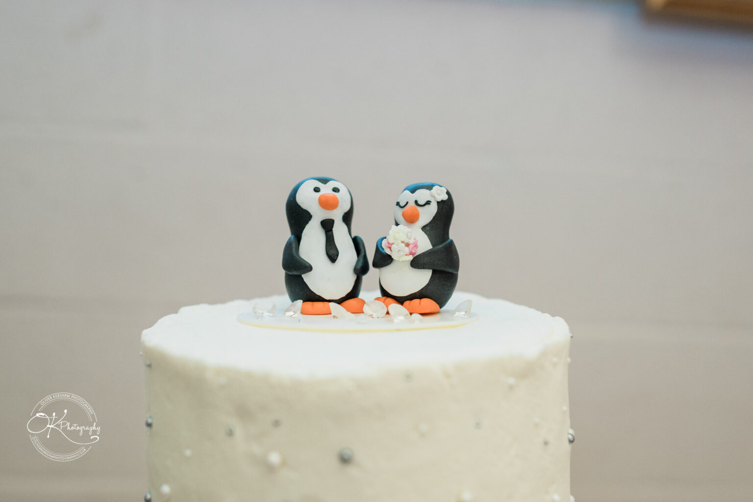 A wedding cake featuring two cute penguin figurines on top, adorned with a flower and intricate decorations.