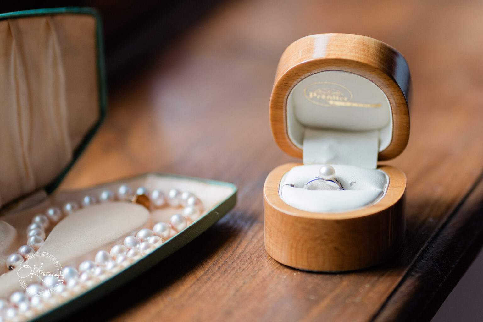 A wooden ring box with a silver ring sits beside a green velvet jewelry case containing a pearl necklace.