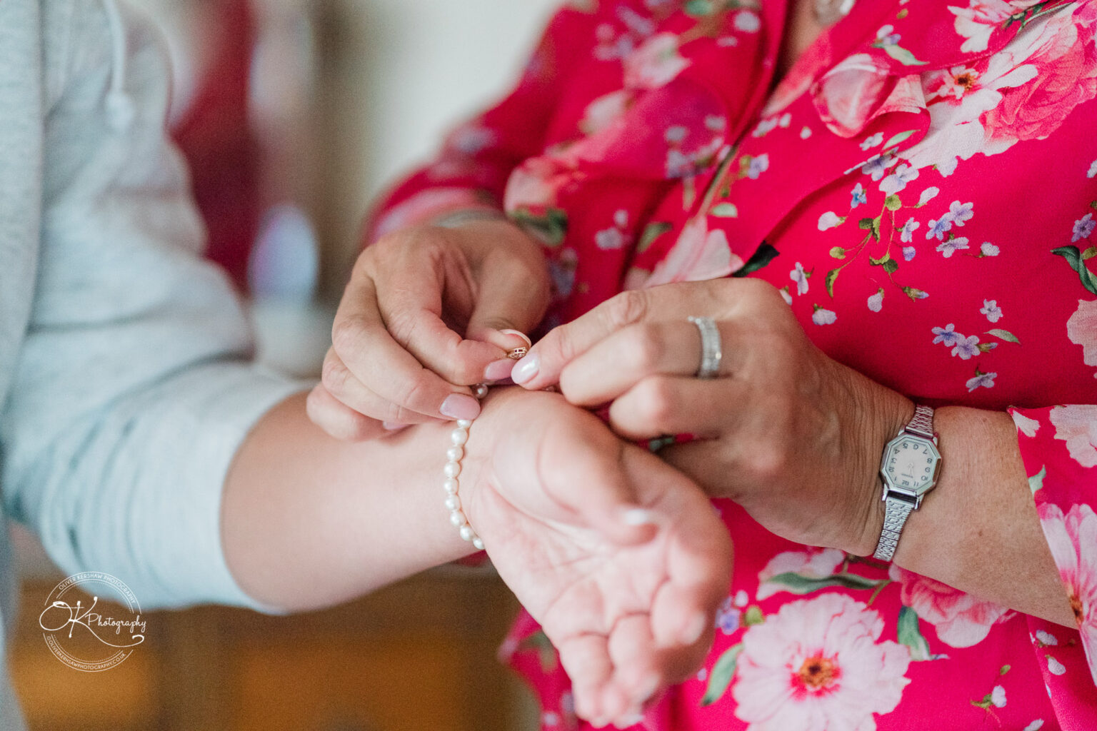 A close-up of two hands, one attaching a bracelet on the wrist of another person, both adorned in floral patterns.