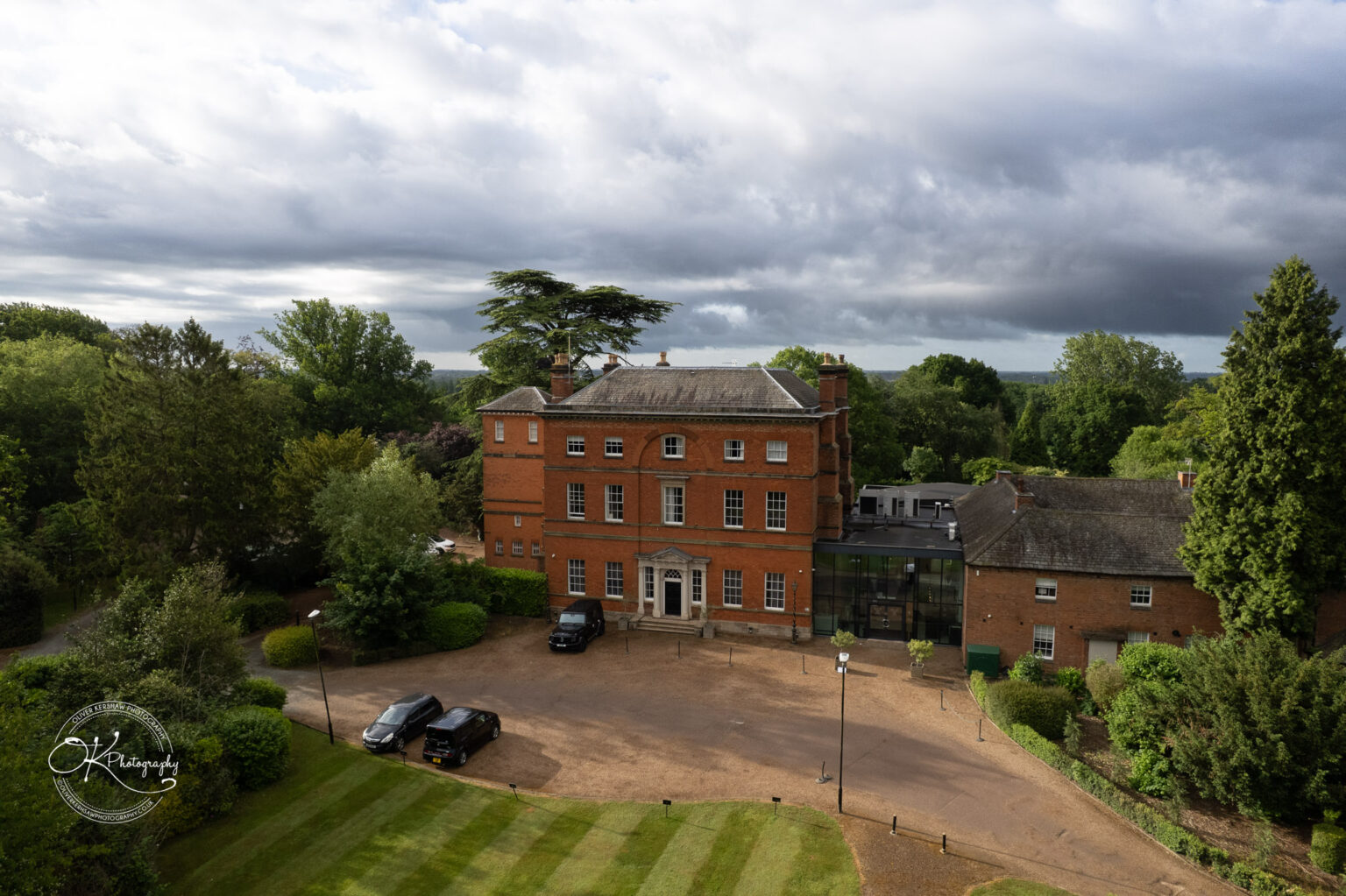 Aerial view of Winstanley House, showcasing its red brick architecture surrounded by greenery and a gravel driveway.