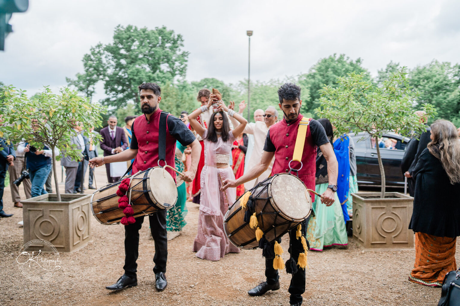 Two drummers in traditional attire engage guests at a Winstanley House wedding, surrounded by attendees in colourful outfits.