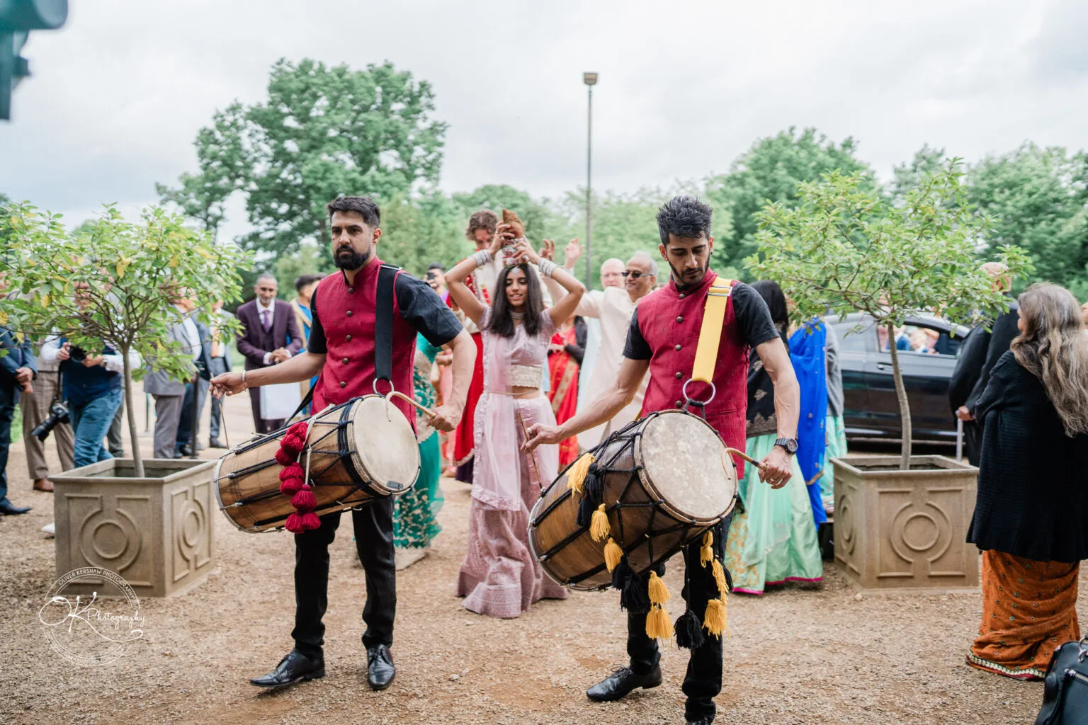 Roshni & Joseph-wedding -Winstanley House-Photography By Oliver Kershaw - OK502025 Two drummers in traditional attire engage guests at a Winstanley House wedding, surrounded by attendees in colourful outfits.
