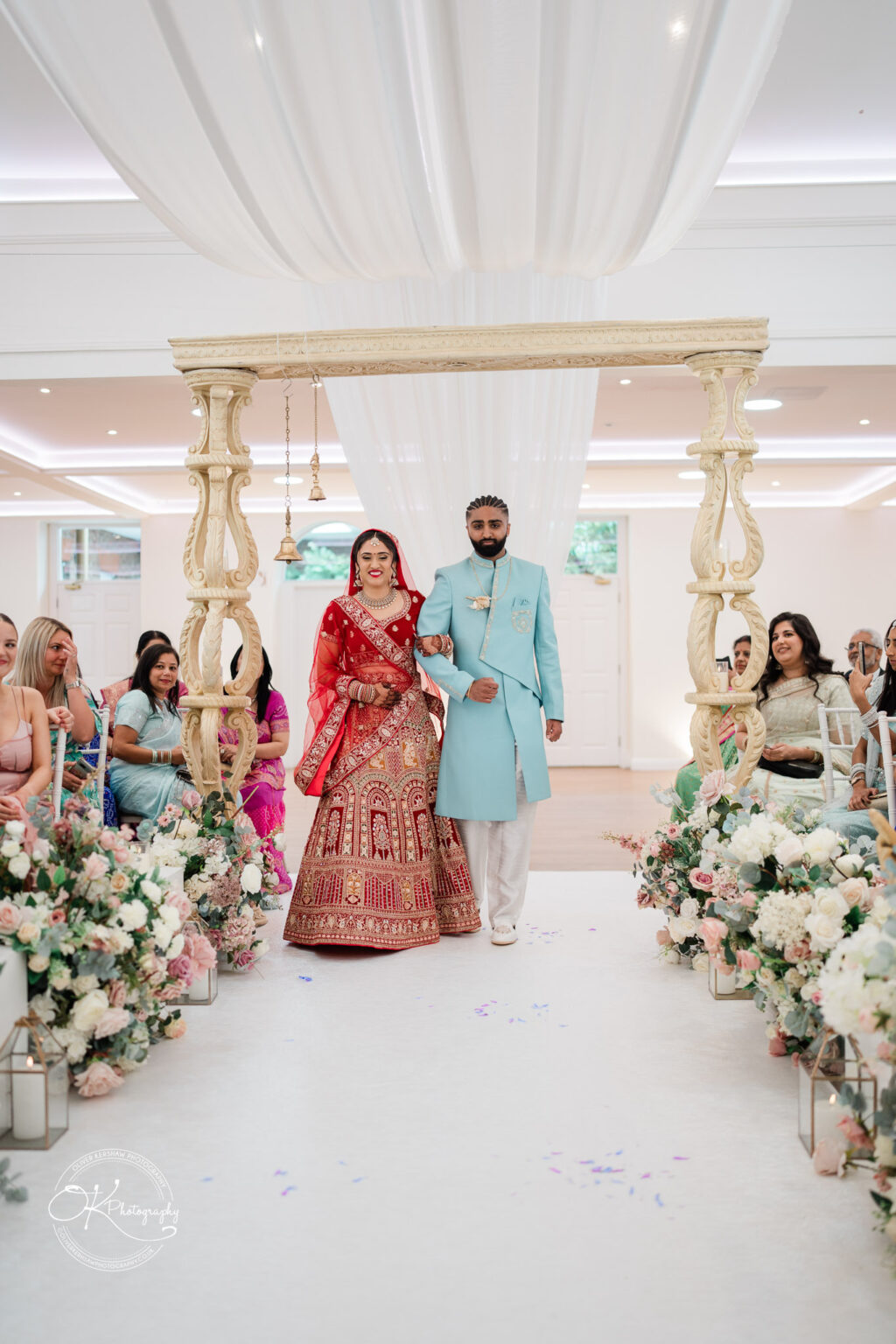 A bride and groom stand under a decorative archway at their wedding ceremony, surrounded by guests and floral arrangements.