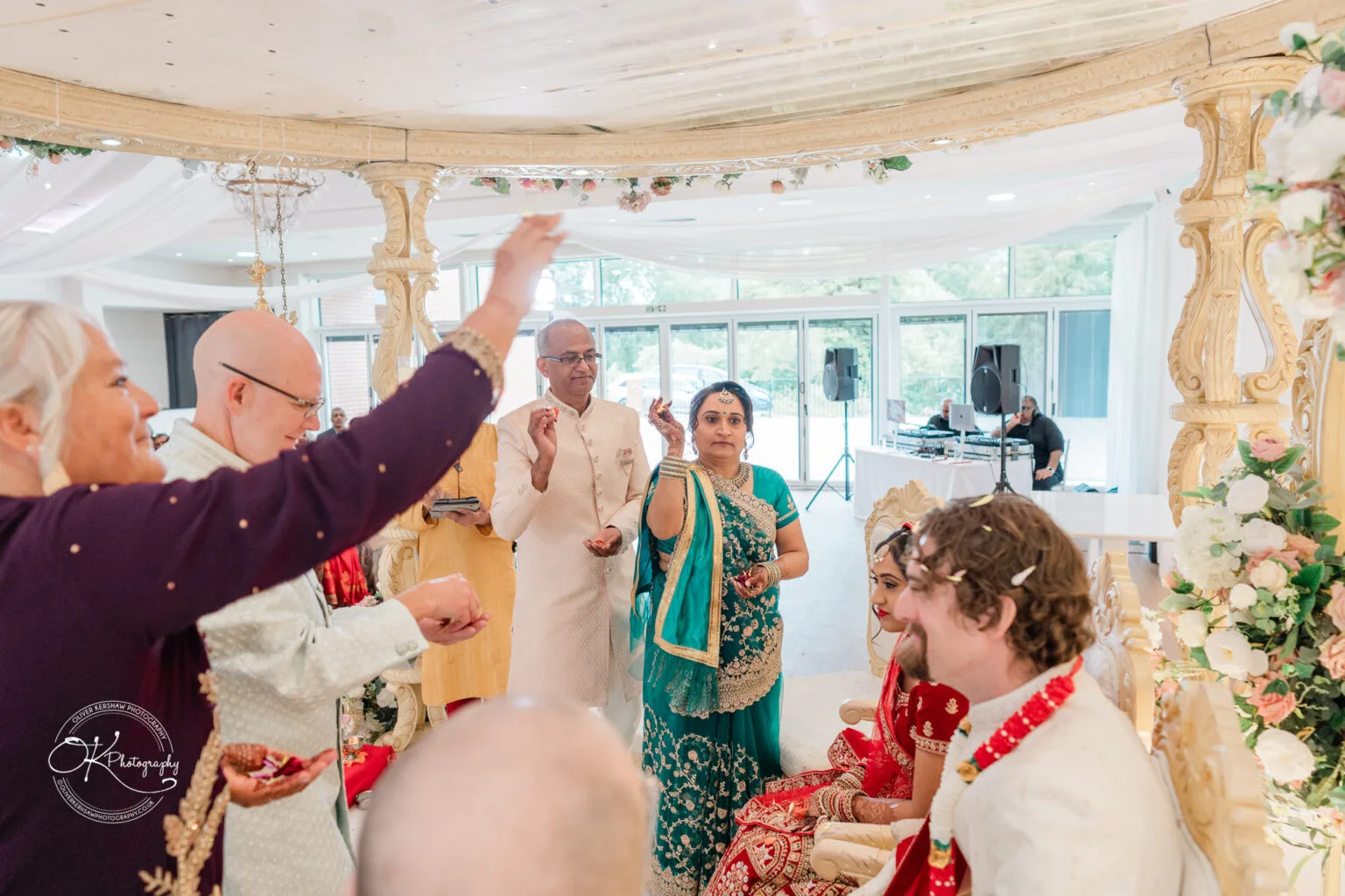 Roshni & Joseph-wedding -Winstanley House-Photography By Oliver Kershaw - OK502403 A joyful wedding ceremony at Winstanley House, featuring a couple adorned in traditional attire, surrounded by guests celebrating.