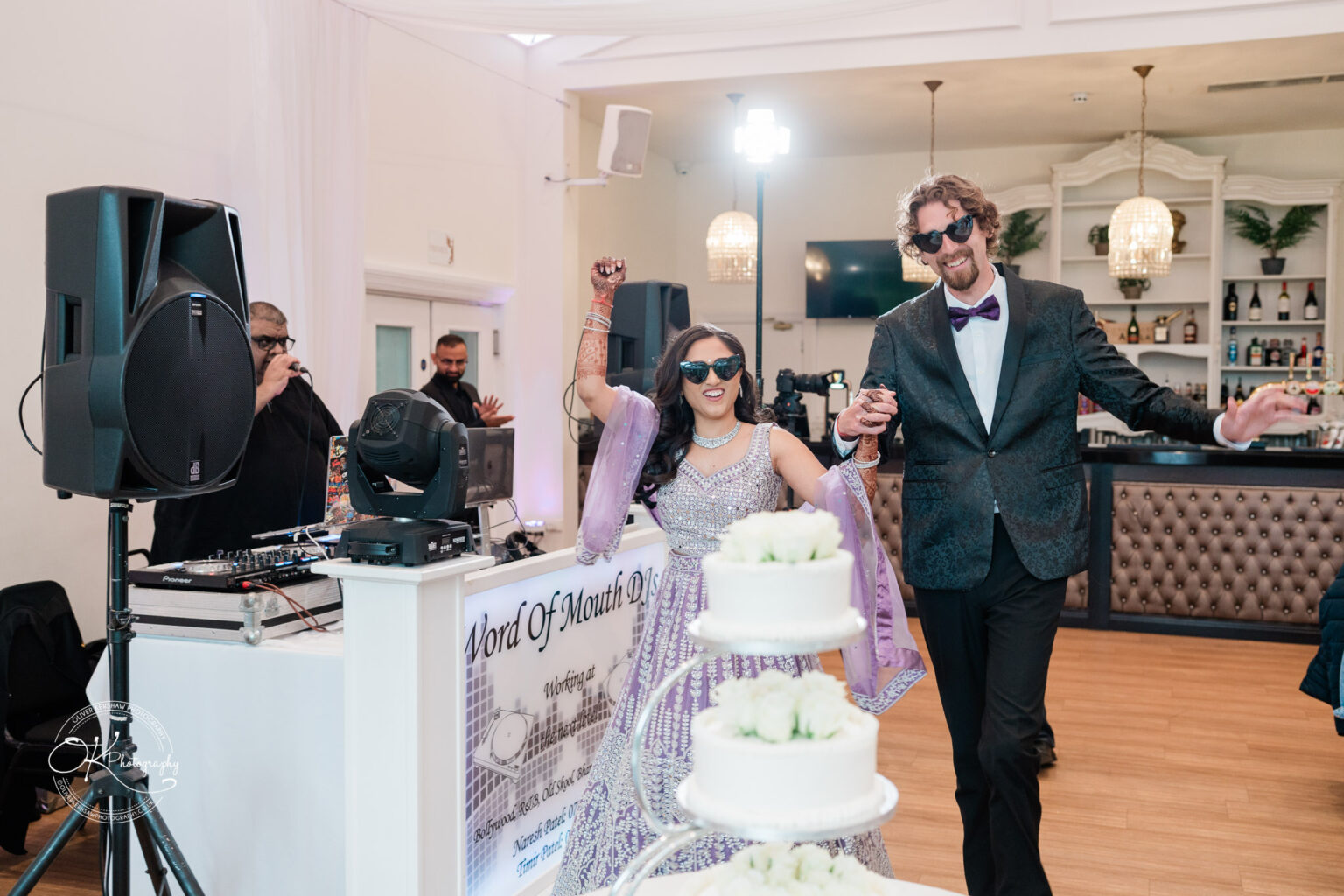 A couple enters a wedding reception at Winstanley House, dressed elegantly, with one wearing sunglasses and holding hands joyfully.