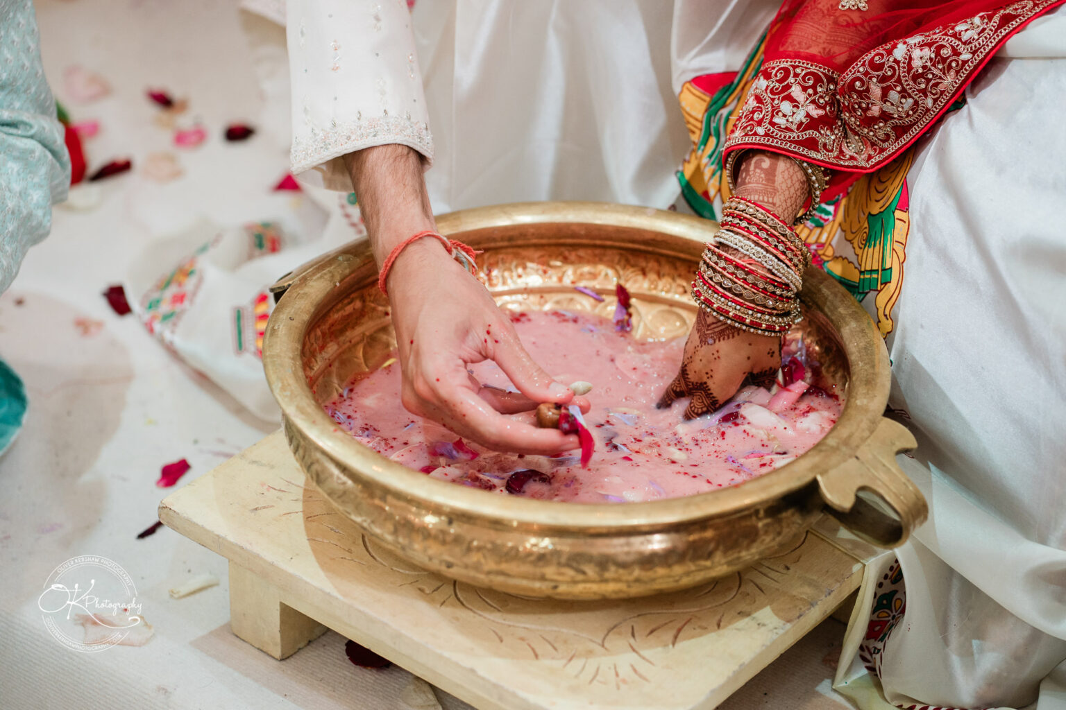 Hands of a bride and groom mixing ingredients in a traditional bowl during a wedding ceremony, adorned with decorative attire and jewelry.